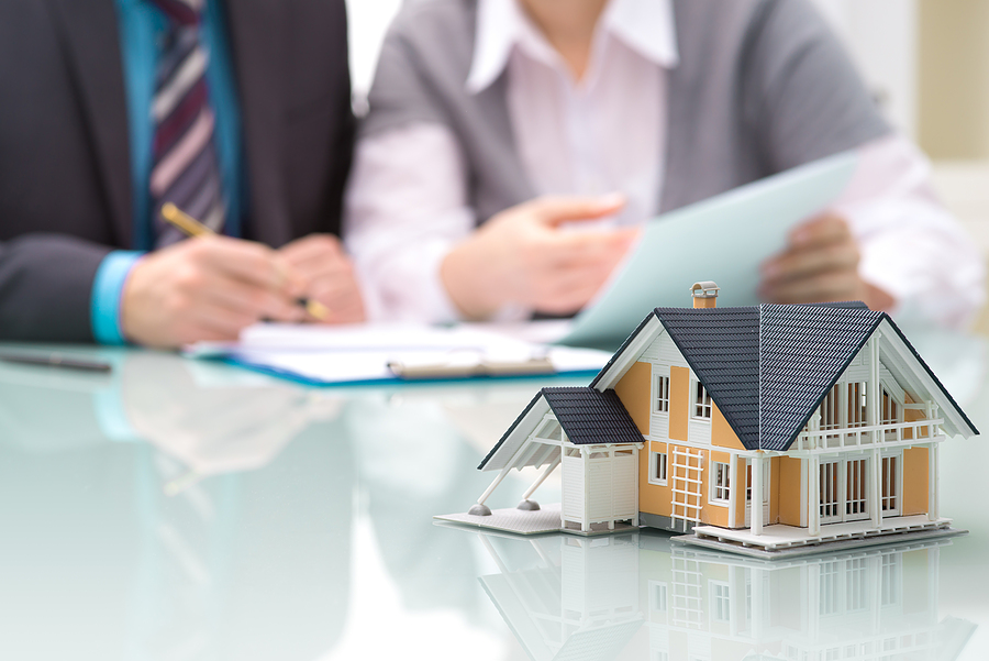 Insurance agent and homeowner go over a homeowners insurance policy with model house in foreground.