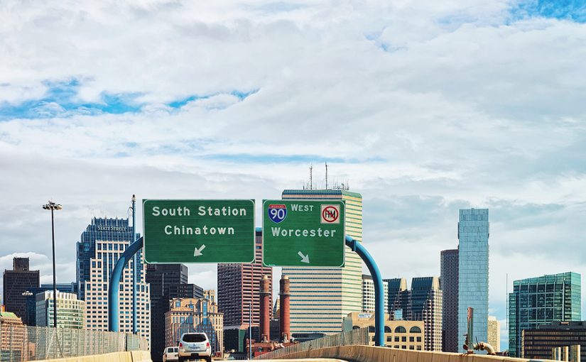 Car on Massachusetts freeway with Boston skyline.