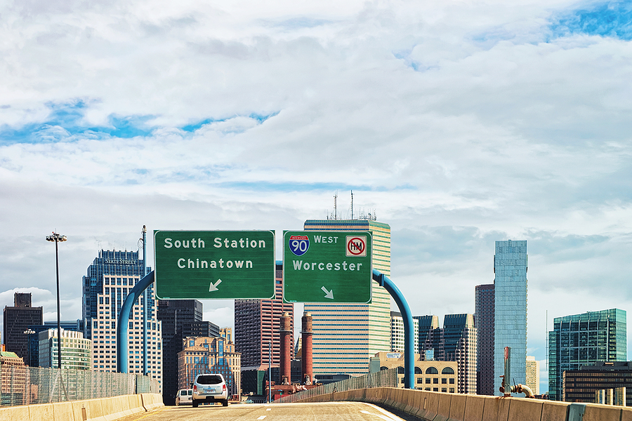 Car on Massachusetts freeway with Boston skyline.