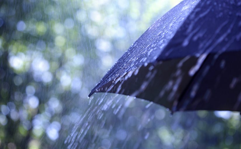 Off-center shot of a black umbrella in the rain.