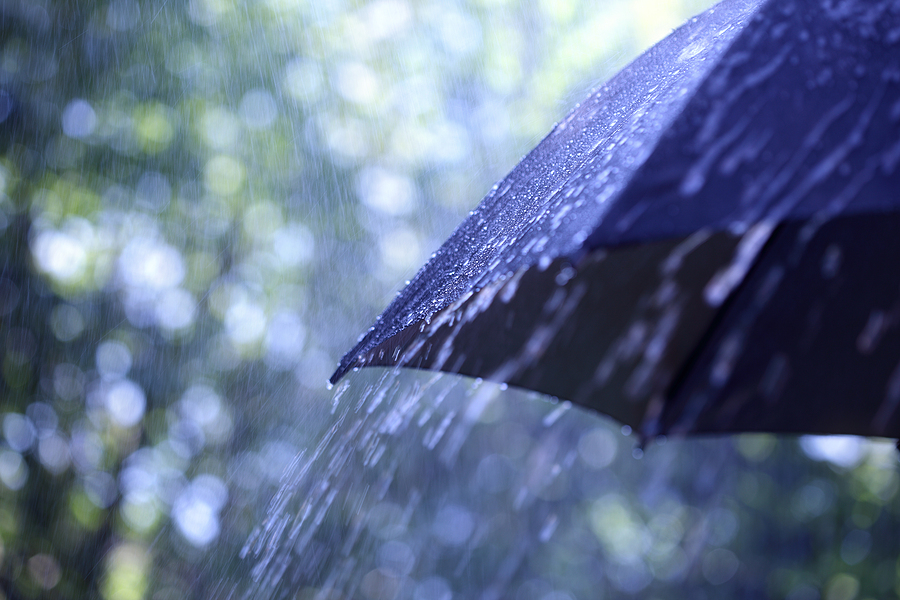 Off-center shot of a black umbrella in the rain.