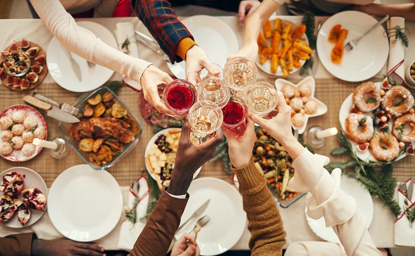 People toast with glasses over dinner table at a holiday party.