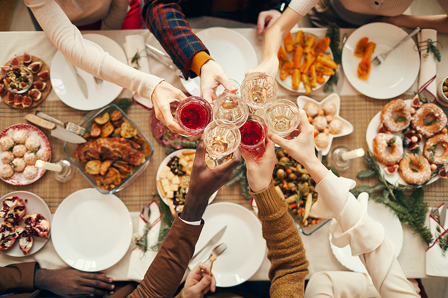 People toast with glasses over dinner table at a holiday party.