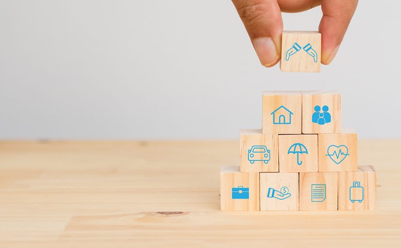 Hand placing wooden block representing liability protections on a stack of insurance assets.