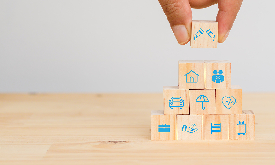 Hand placing wooden block representing liability protections on a stack of insurance assets.