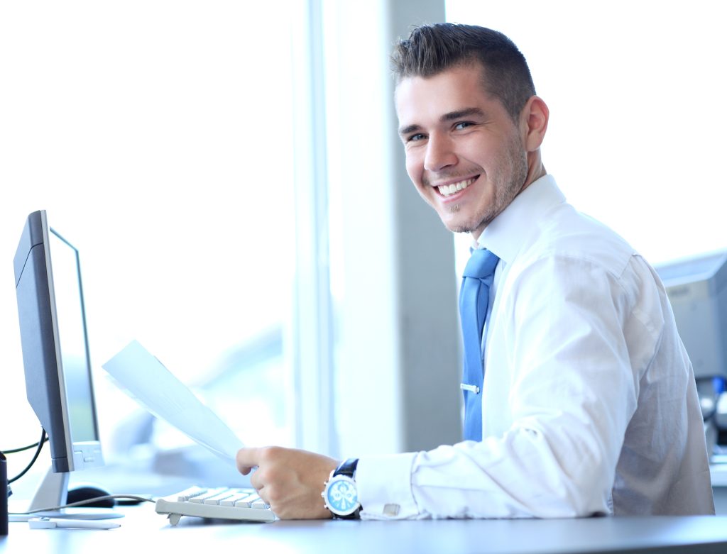 Smiling businessman in a company office using a computer.