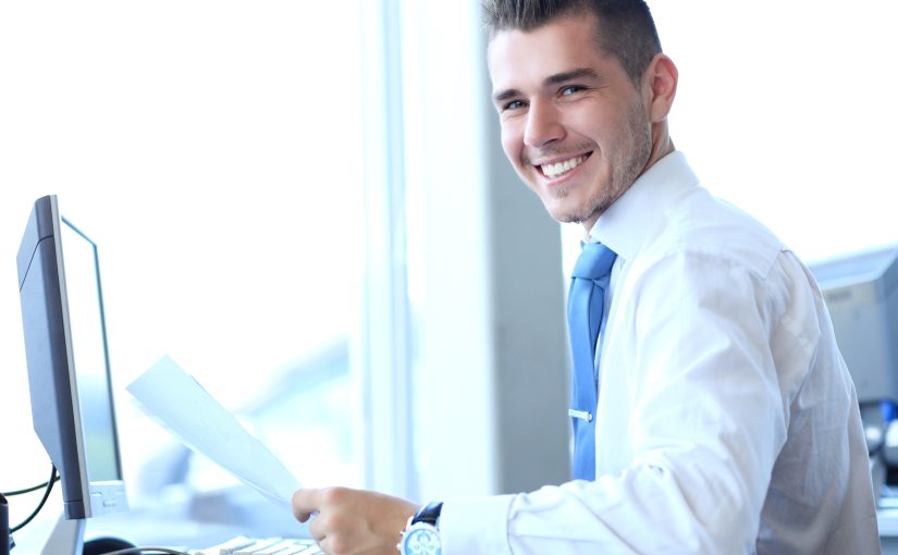 Smiling businessman in a company office using a computer.