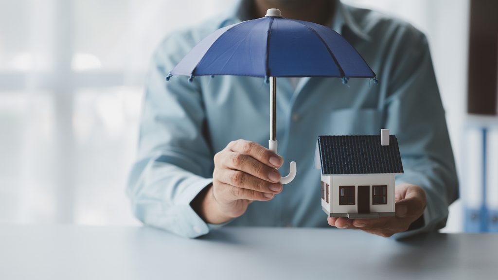 Individual holding an umbrella over a model of a house to represent umbrella insurance.