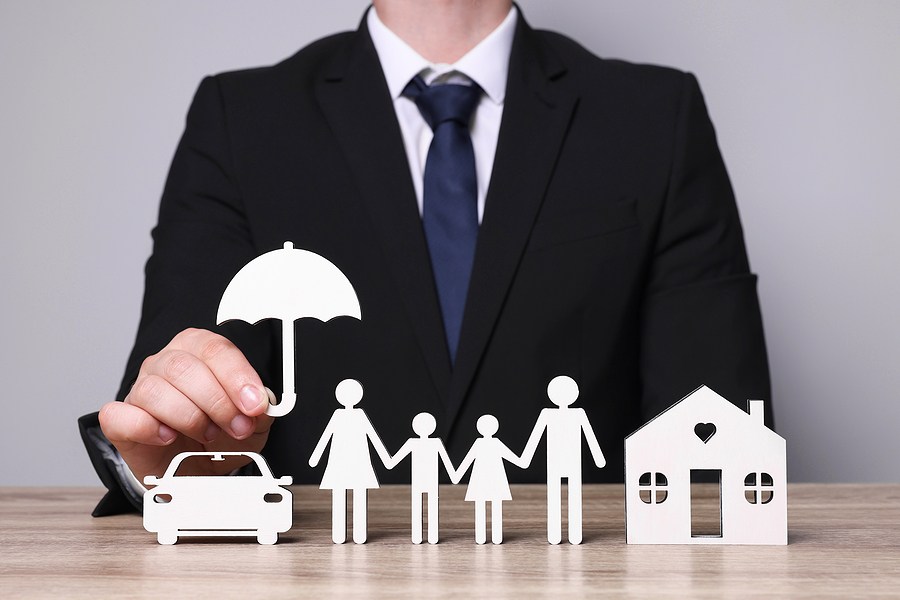 Man in suit holding umbrella over cutouts of a car, house, and family.