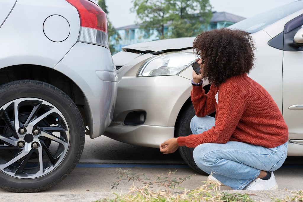 Driver on call with insurance agent in front of rear-end auto accident.