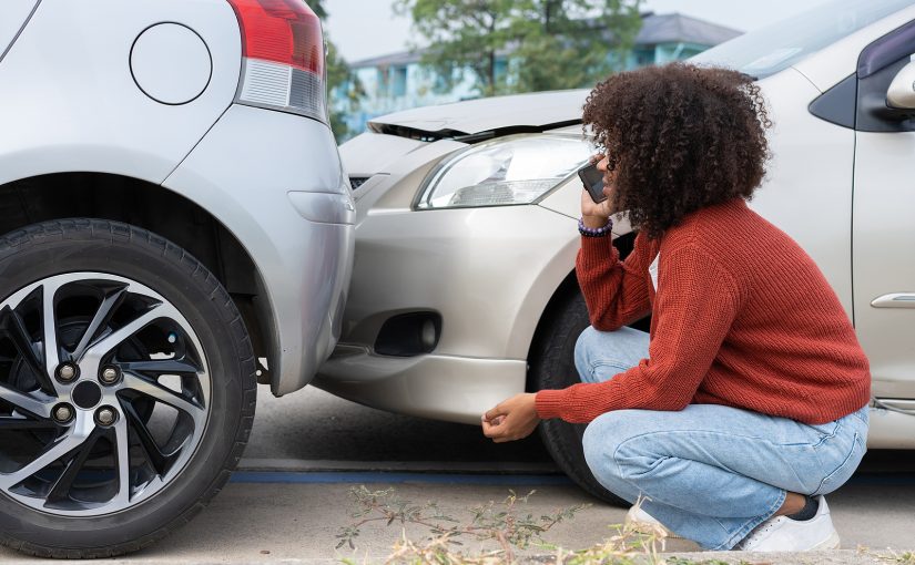 Driver on call with insurance agent in front of rear-end auto accident.