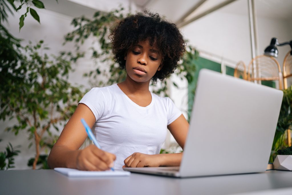 Woman in house taking a home inventory with use of a notepad and laptop.