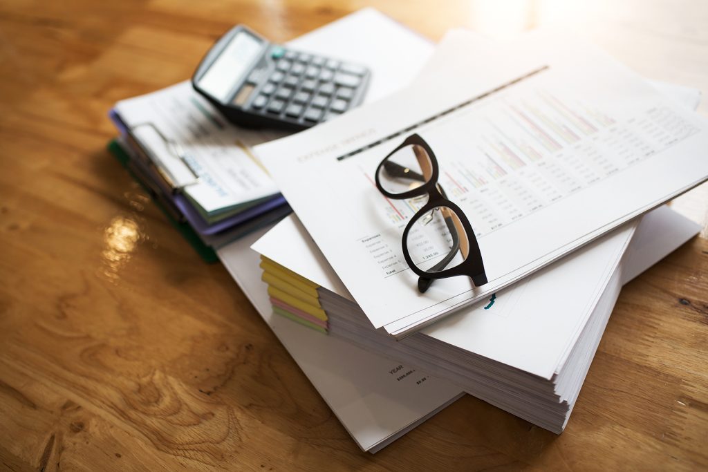 A collection of business documents on a desk with a pair of glasses resting on them.