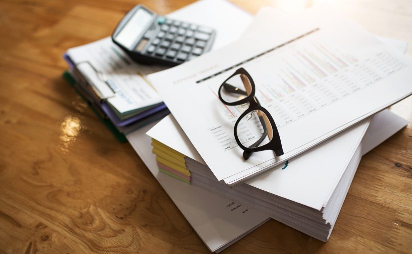 A collection of business documents on a desk with a pair of glasses resting on them.