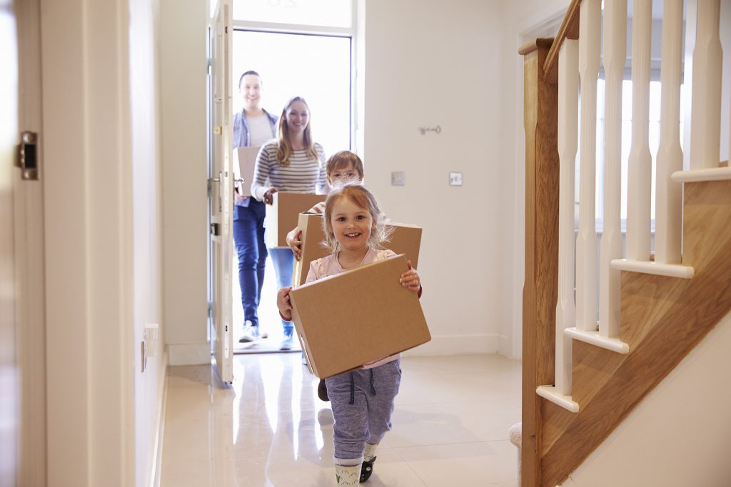 Family moving into a new home, carrying moving boxes.