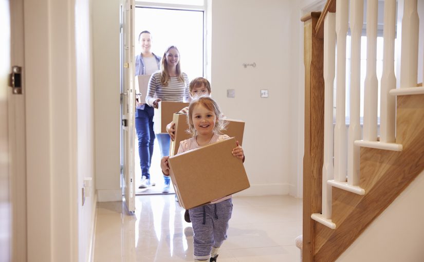 Family moving into a new home, carrying moving boxes.