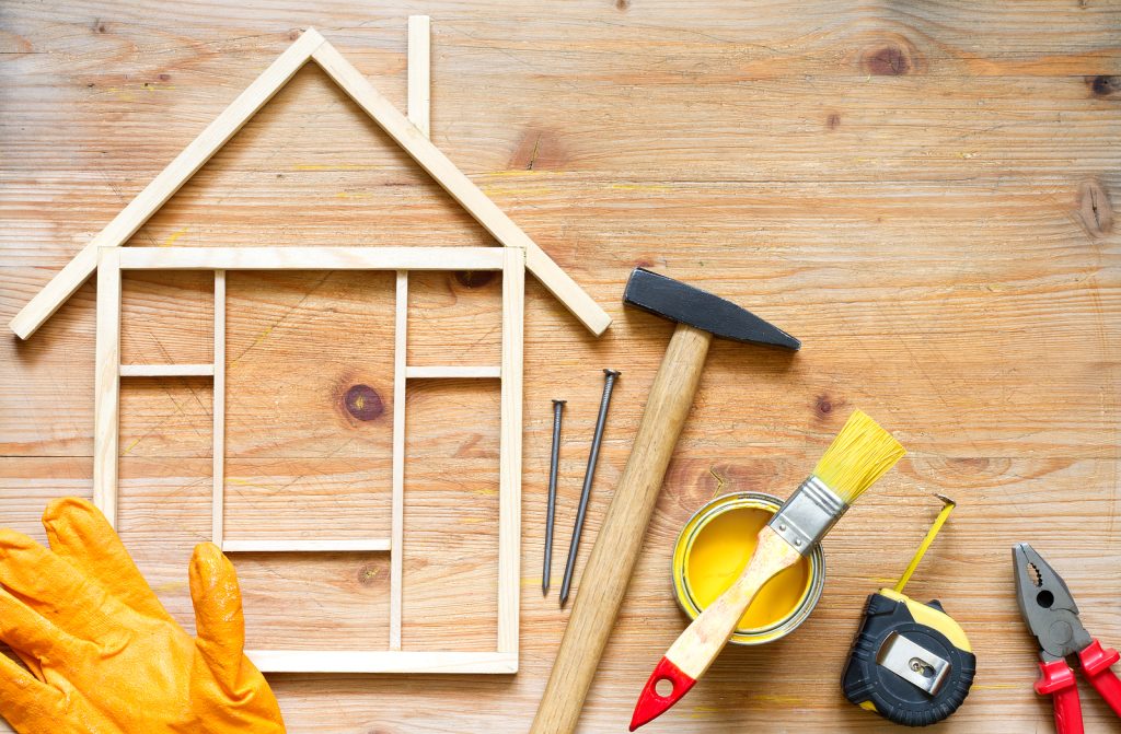 Wooden frame representing a house with hammer, paint, and other home renovation tools.