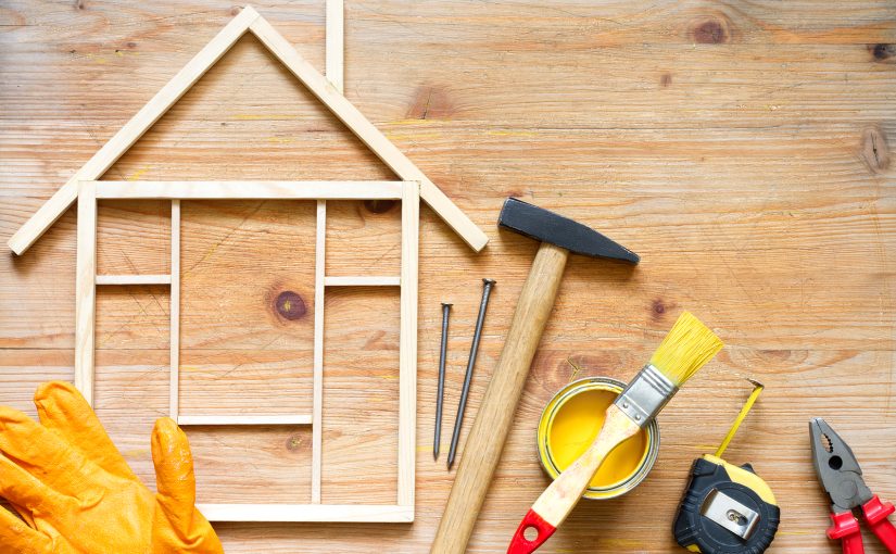 Wooden frame representing a house with hammer, paint, and other home renovation tools.