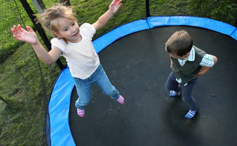 Two children jumping on trampoline outside