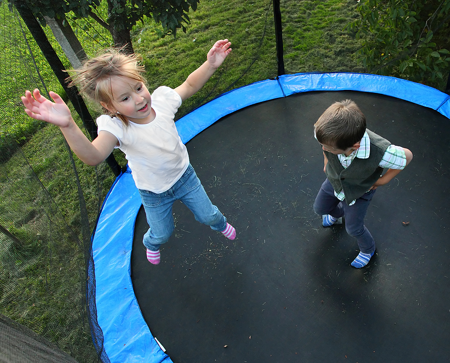 Two children jumping on trampoline outside