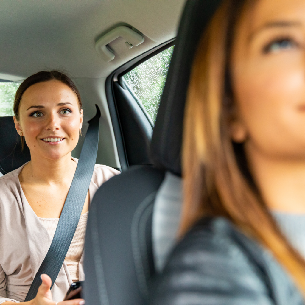 One woman is driving and checking on the other woman through the rearview mirror who is riding in the backseat.