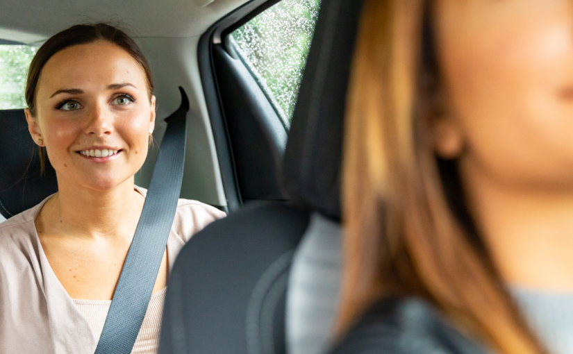 One woman is driving and checking on the other woman through the rearview mirror who is riding in the backseat.