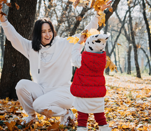 This picture shows a mom and daughter throwing and playing in the fall leaves.