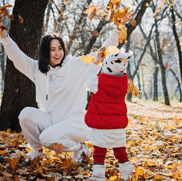 This picture shows a mom and daughter throwing and playing in the fall leaves.