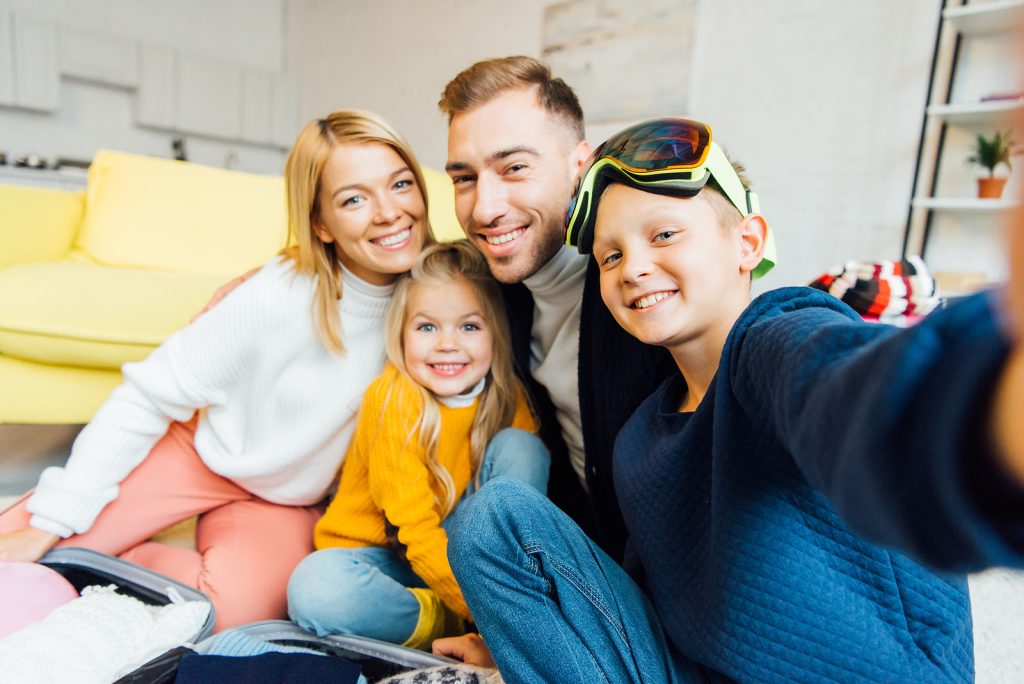 Family of four packing for a holiday vacation, smiling together for a selfie.