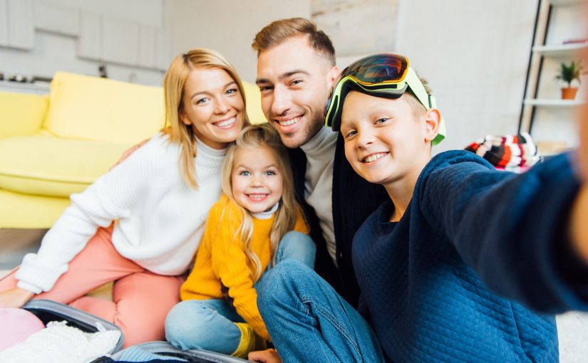 Family of four packing for a holiday vacation, smiling together for a selfie.