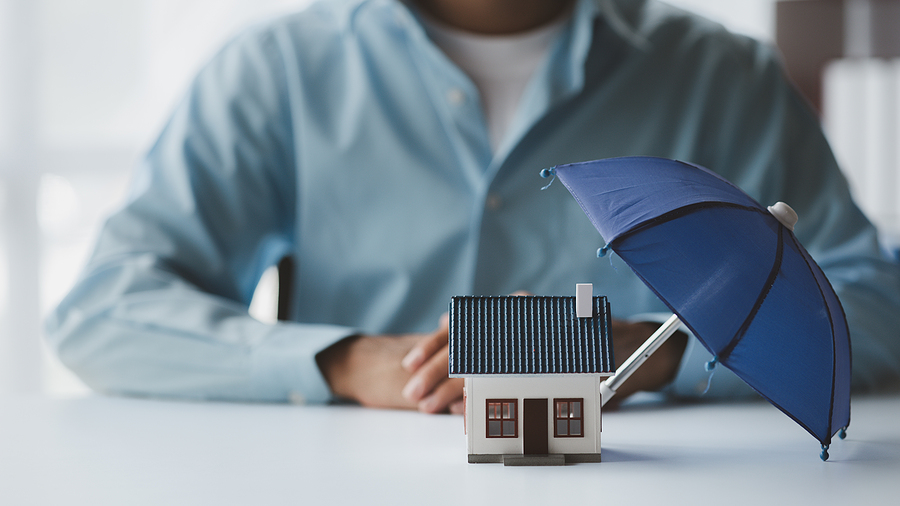 House with an umbrella propped over the roof, representing umbrella insurance.